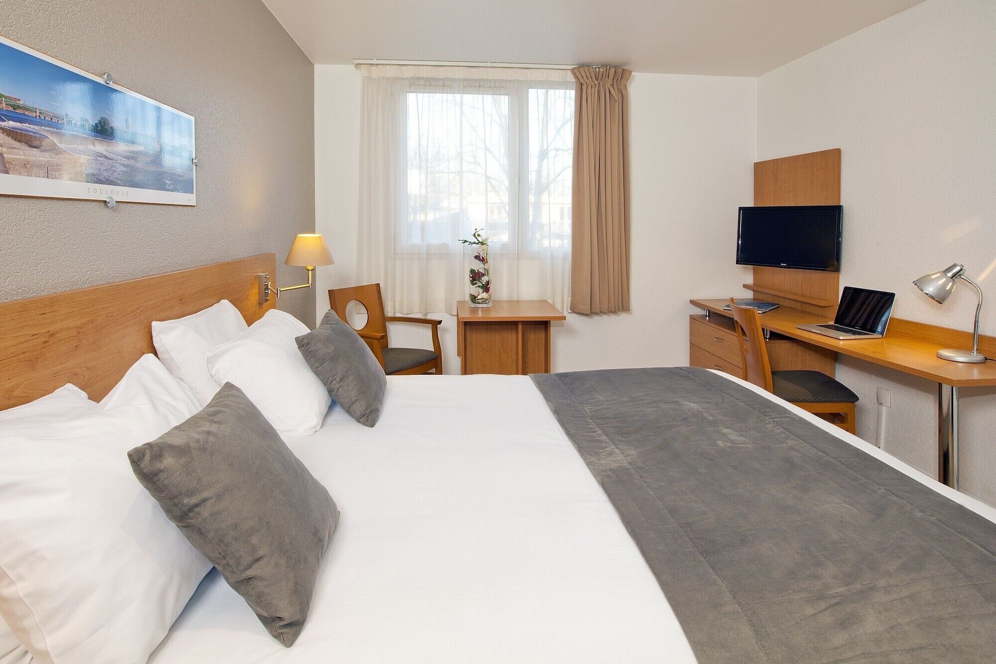 A hotel room with a large bed, a desk with a computer, a TV, and a lamp.