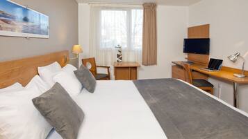 A hotel room with a large bed, a desk with a computer, a TV, and a lamp.