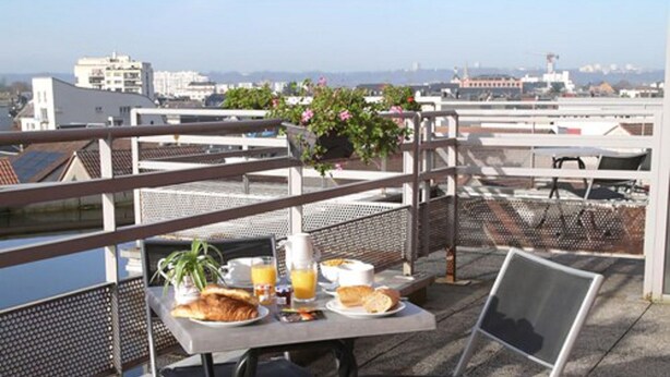 A table with breakfast items, a chair, and a railing overlooking a cityscape. - Séjours & Affaires Rouen Normandie (Sotteville-les-Rouen)