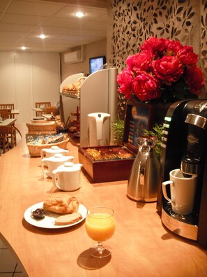 A breakfast buffet with various food items, a coffee machine, and a vase of red flowers.