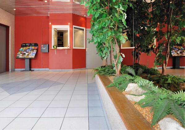 A lobby with a red wall, a reception desk, a directory, and indoor plants.