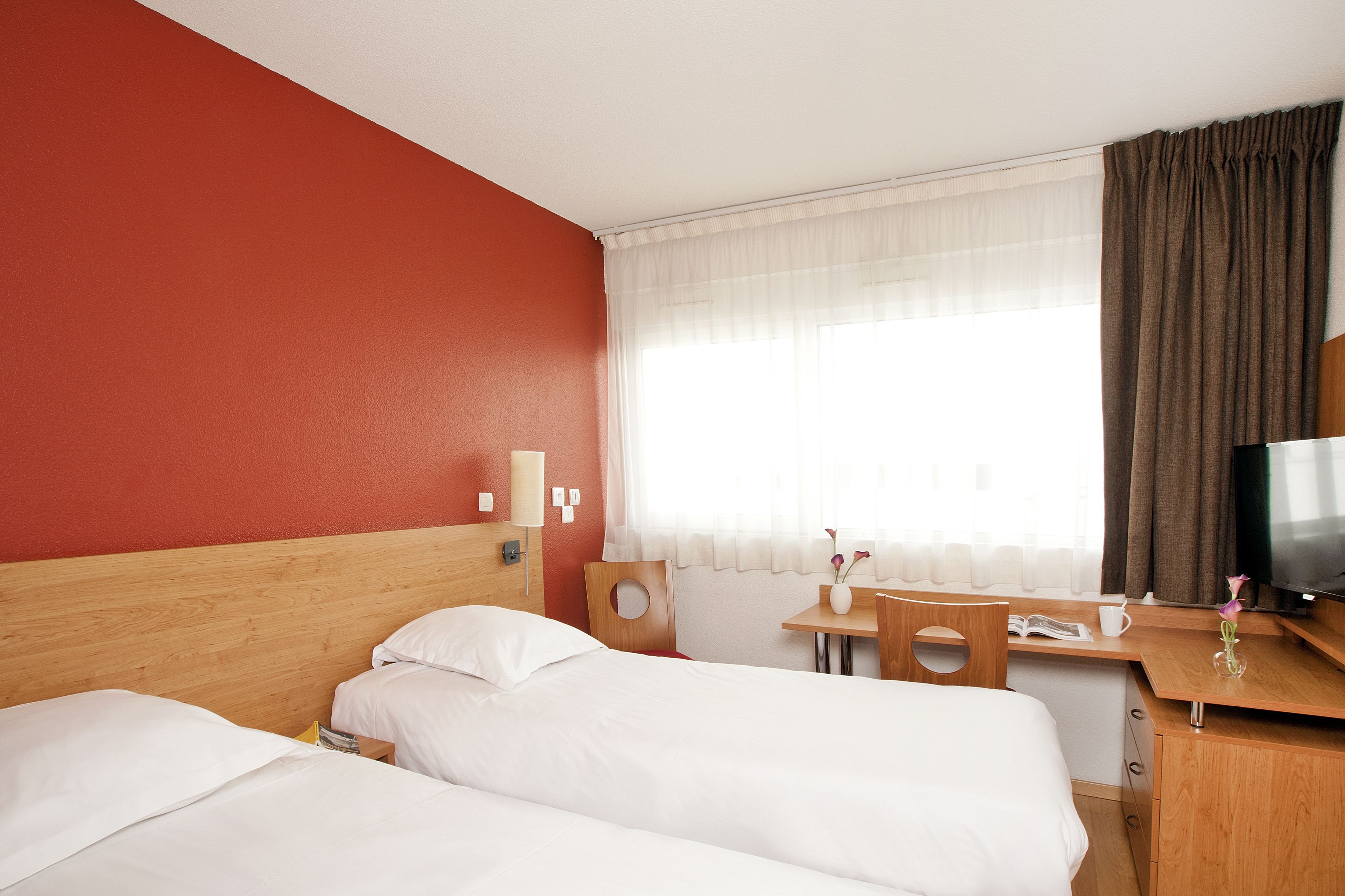 A hotel room with two beds, a wooden desk, a television, and a window with curtains.