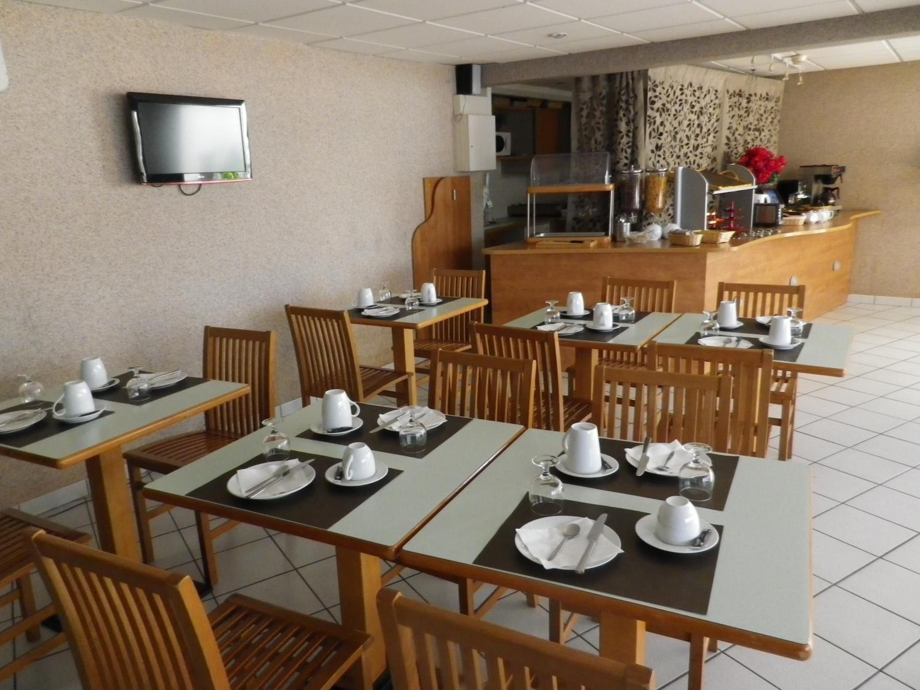 A dining area with multiple tables set for breakfast, a television mounted on the wall, and a kitchen area in the background.