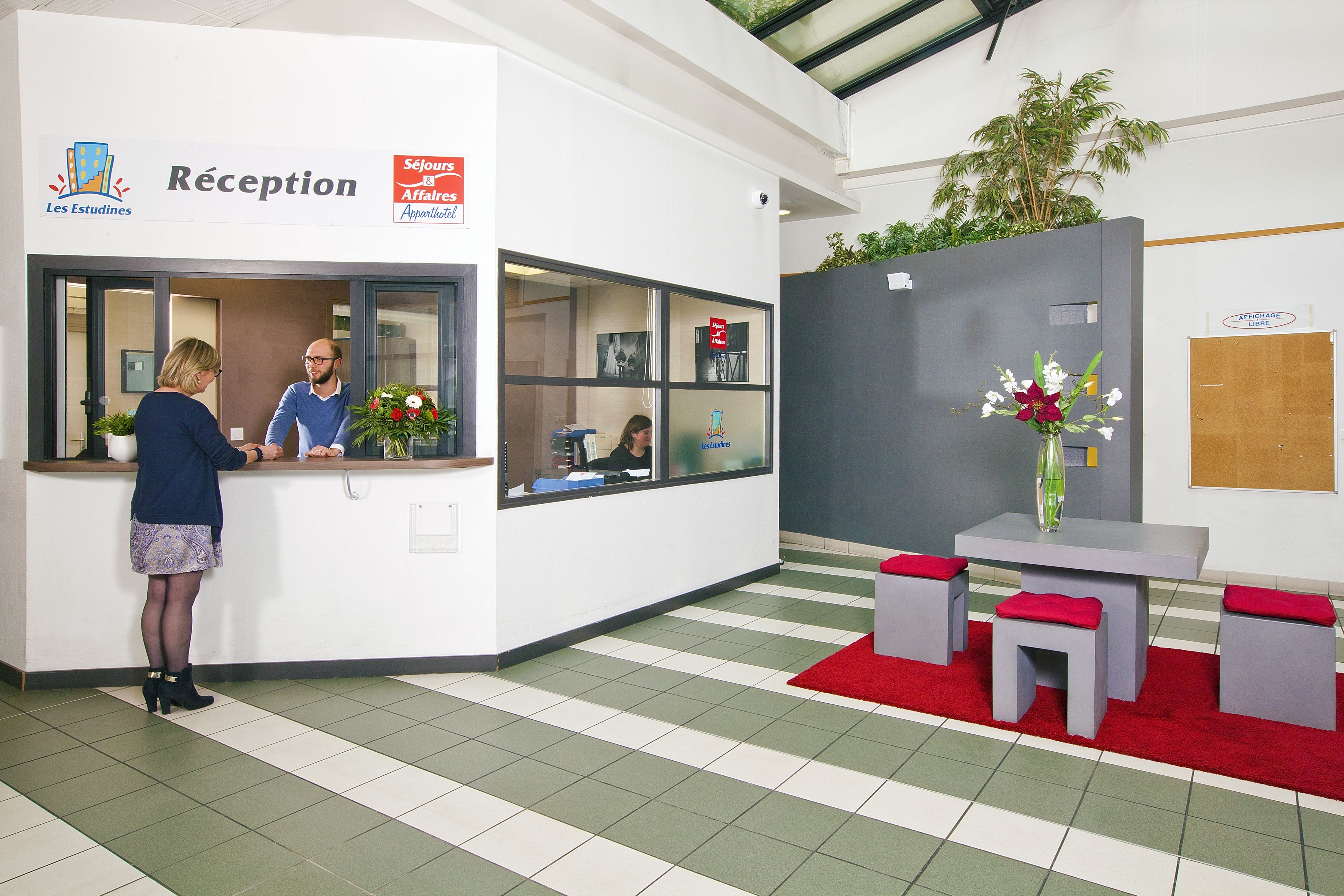 A reception area with a check-in counter, a seating area with a red rug, and a potted plant.