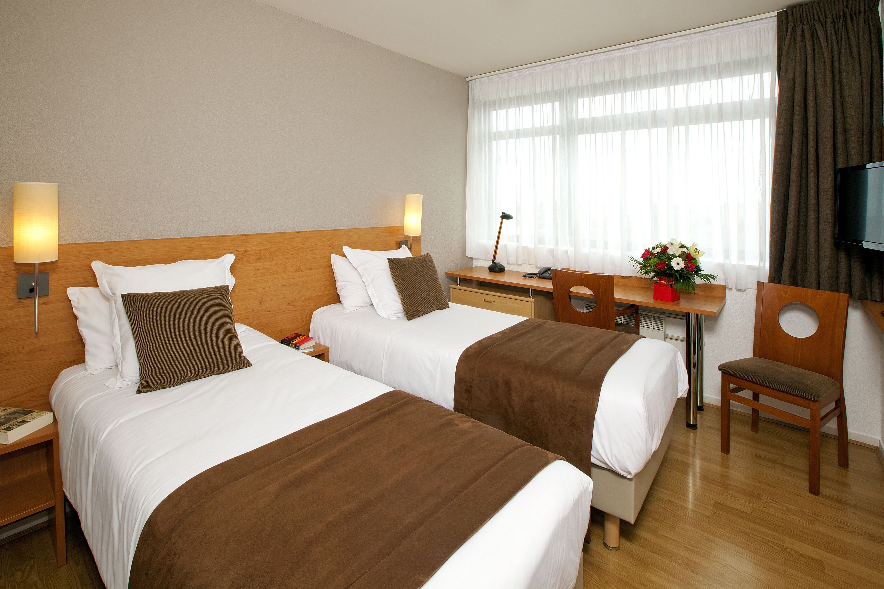 Een hotelkamer met twee bedden, een bureau met stoel, een televisie en een raam met gordijnen.