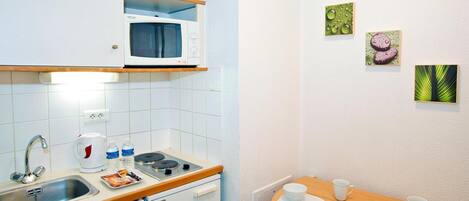 A compact kitchen with a microwave, sink, and a small dining table set with cups and plates.
