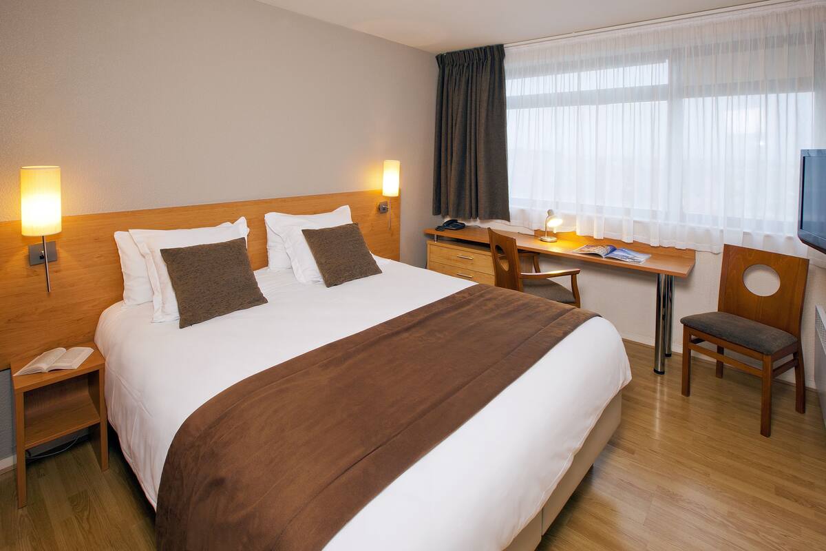 Een hotelkamer met een groot bed, nachtkastjes, een bureau en een stoel.