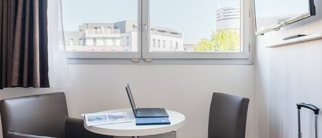 A room with a table, two chairs, a laptop, a suitcase, and a TV on the wall.