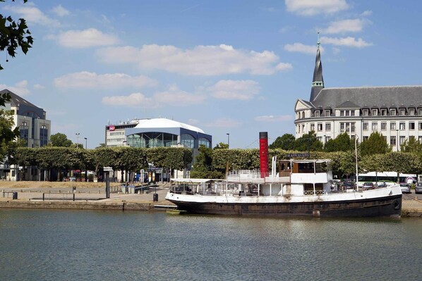 A river with a boat docked near a modern building with a glass facade and a traditional building with a spire. - Sejours & Affaires Nantes Ducs de Bretagne (Nantes)