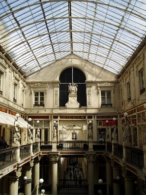 Ein mehrgeschossiges Gebäude mit Glasdach, aufwändigen Statuen und klassischer Architektur.