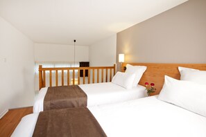 Ein Hotelzimmer mit zwei Betten, Holz-Kopfteilen, weißer Bettwäsche, einem Nachttisch mit Lampe und Blick auf den Balkon.