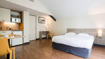 A compact hotel room with a kitchenette, a bed, a desk, and a chair.