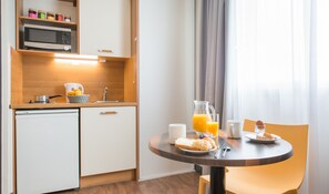 A compact kitchen with a microwave, sink, and a small refrigerator. There is a dining table with breakfast items like bread, a jug of orange juice, and a glass of water. - Comfort Aparthotel Saint-Nazaire Les Portes de l Ocean (Saint-Nazaire)