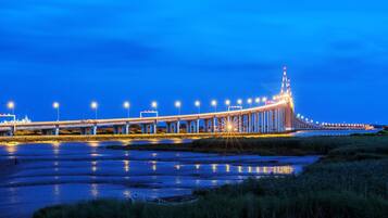 Eine lange Brücke mit gleichmäßig verteilten Lichtern und einem zentralen Turm, die über ein Gewässer führt.