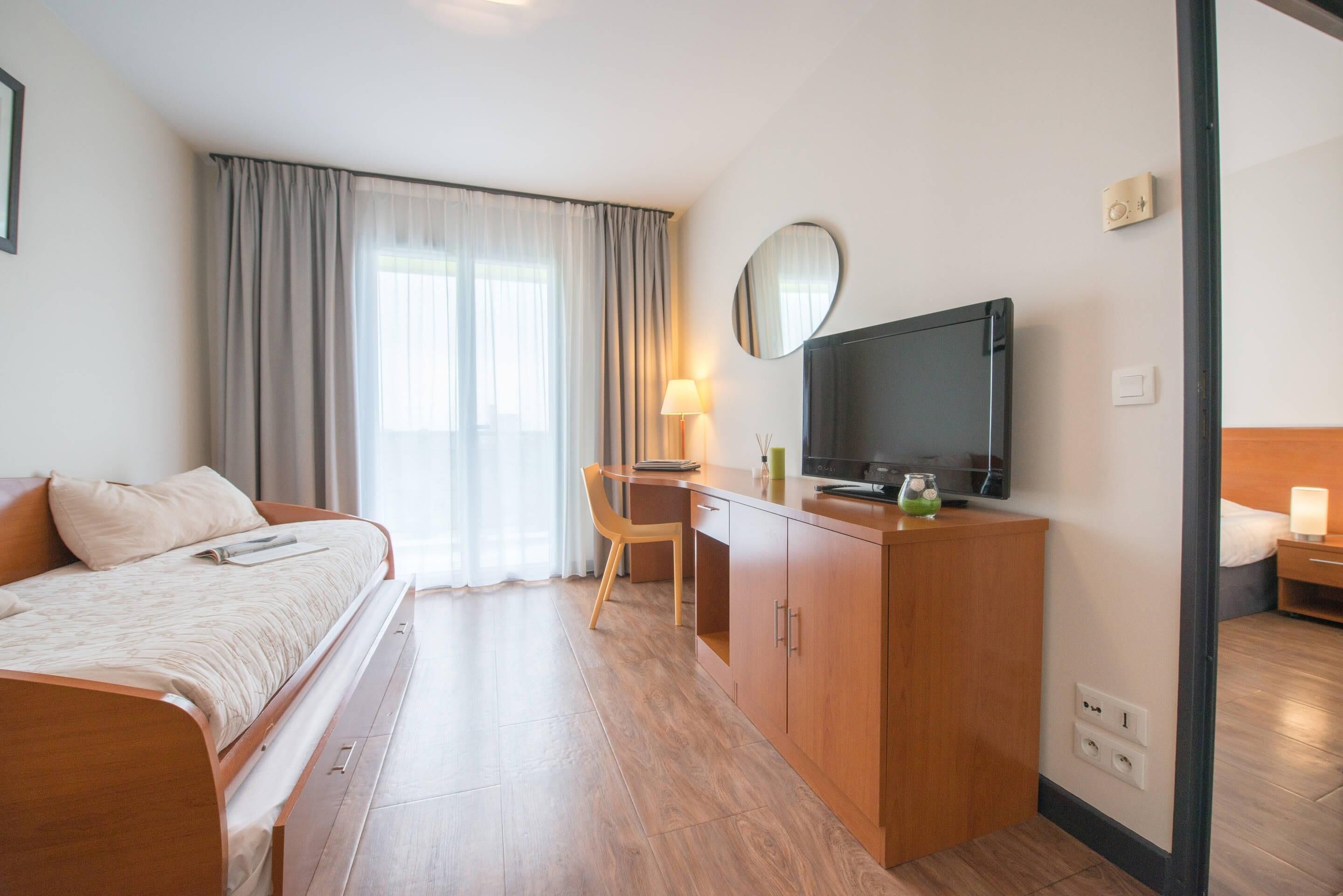 A hotel room with a bed, desk, TV, and a view of the outdoors.