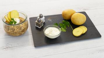 A food arrangement with a jar, two potatoes, a bowl of sauce, and a salt shaker on a slate board.