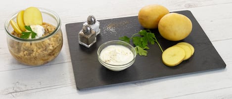 A food arrangement with a jar, two potatoes, a bowl of sauce, and a salt shaker on a slate board.