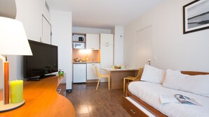 A compact hotel room with a television, a dining table with chairs, a kitchenette, and a bed. - Comfort Aparthotel Saint-Nazaire Les Portes de l Ocean (Saint-Nazaire)