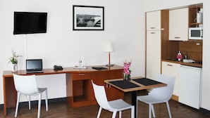 A compact hotel room with a wooden desk, two white chairs, a small table, a TV, a framed picture, a lamp, a microwave, and a mini-fridge. - Comfort Aparthotel Saint-Nazaire Les Portes de l Ocean (Saint-Nazaire)