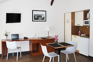 A compact hotel room with a wooden desk, two white chairs, a small table, a TV, a framed picture, a lamp, a microwave, and a mini-fridge. - Comfort Aparthotel Saint-Nazaire Les Portes de l Ocean (Saint-Nazaire)