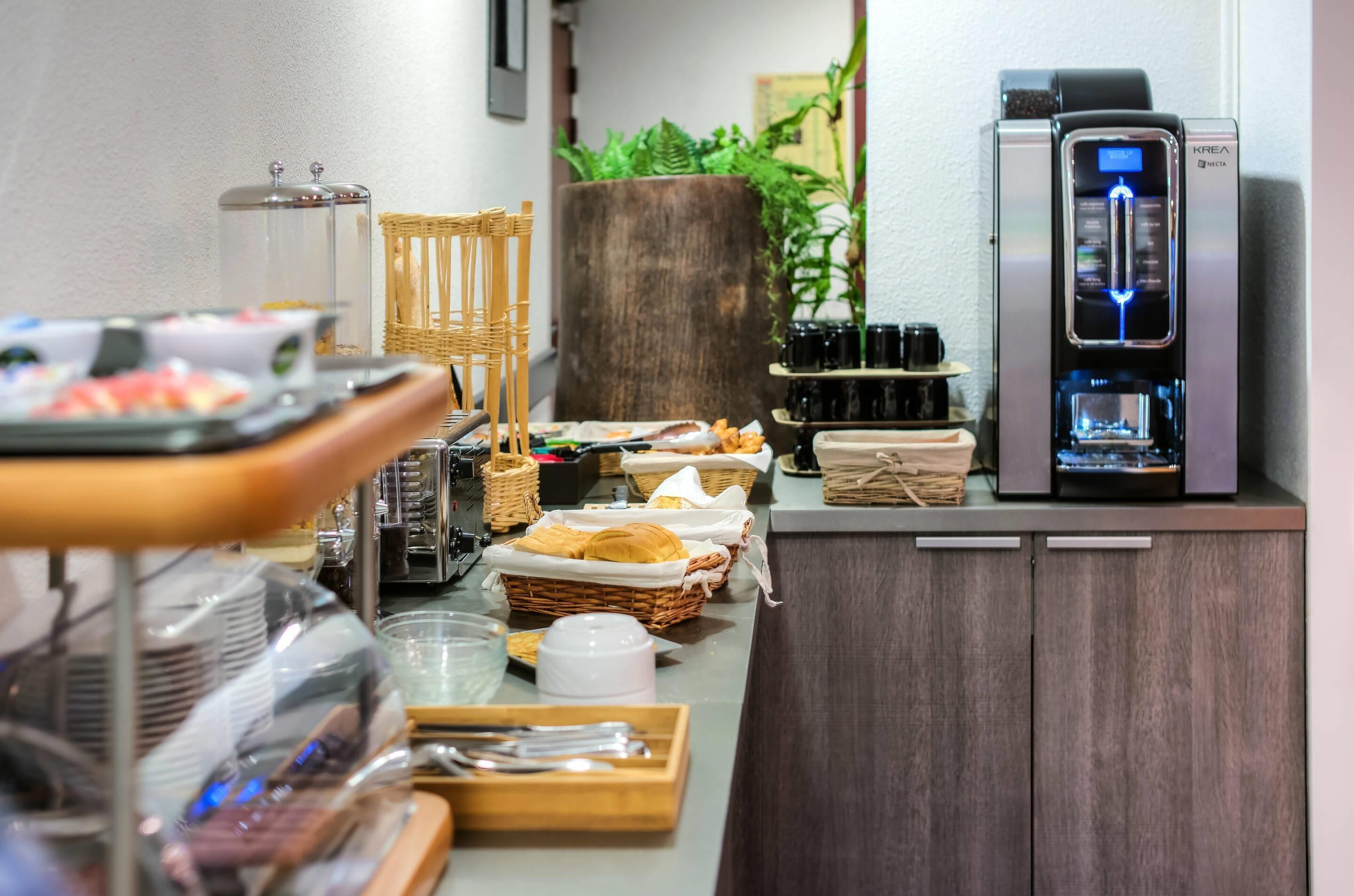 A buffet setup with various food items, a coffee machine, and a large plant.