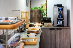 A buffet setup with various food items, a coffee machine, and a large plant.