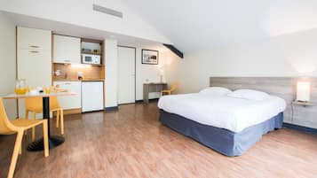 A compact hotel room with a kitchenette, a dining area, and a bed.