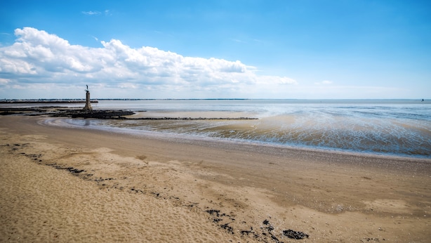A beach with a lighthouse, sandy shore, and calm sea under a clear sky. - Comfort Aparthotel Saint-Nazaire Les Portes de l Ocean (Saint-Nazaire)