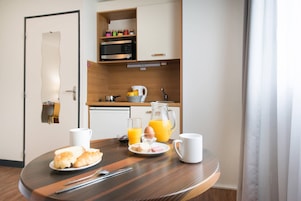 Uma mesa de café da manhã com croissants, um prato de doces, um jarro de suco de laranja e uma xícara de café.