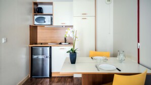 A compact kitchen with a refrigerator, microwave, and wooden cabinets. There's a dining table with chairs and a potted orchid. - Comfort Aparthotel Saint-Nazaire Les Portes de l Ocean (Saint-Nazaire)