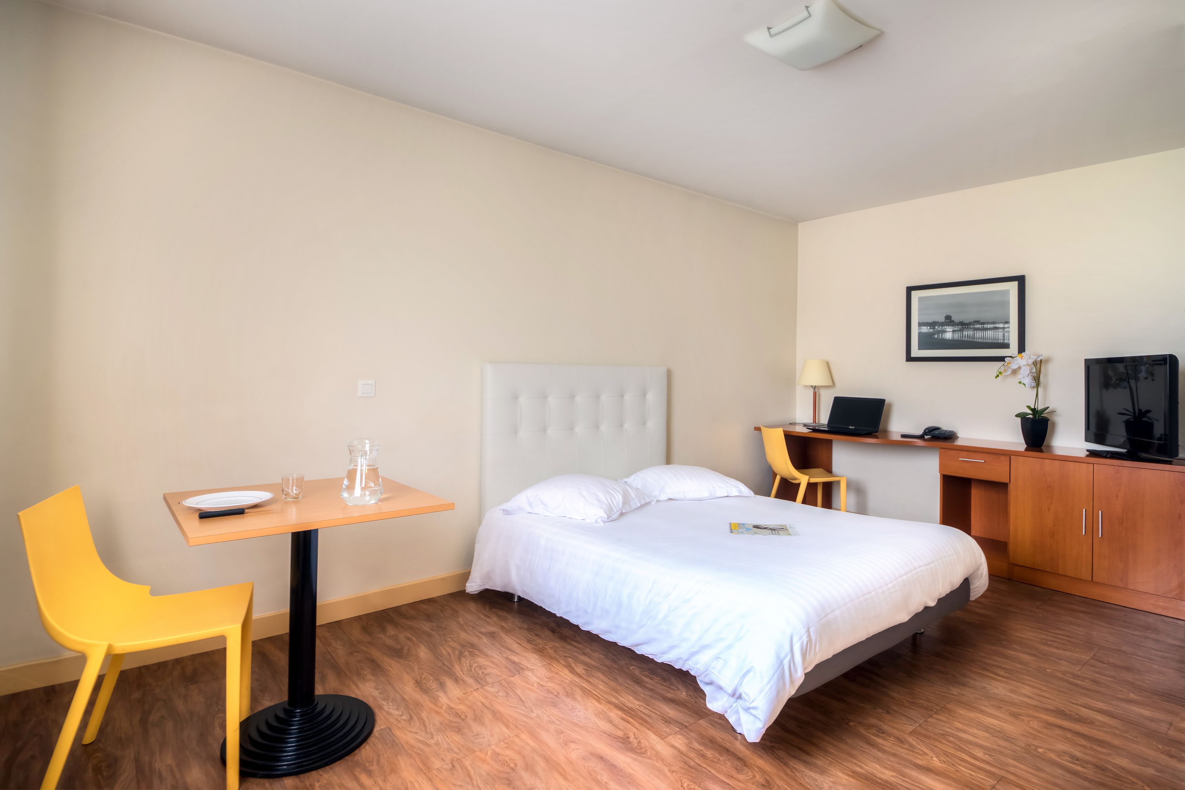 Ein Hotelzimmer mit einem Bett, einem Schreibtisch, einem Sessel, einem Fernseher und einem gerahmten Bild an der Wand.