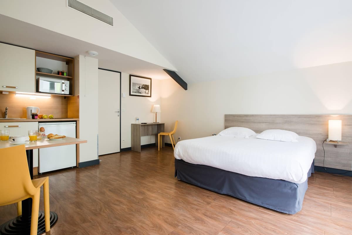 A compact hotel room with a kitchenette, a bed, a desk, and a chair.