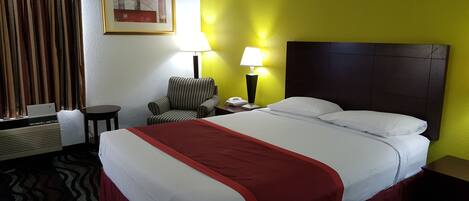 A hotel room with a bed, a chair, a desk, a lamp, and a painting on the wall.