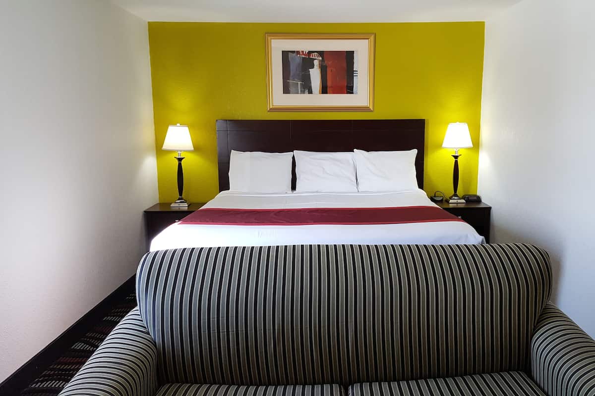 A hotel room with a bed, two bedside lamps, a framed artwork above the bed, and a striped sofa.