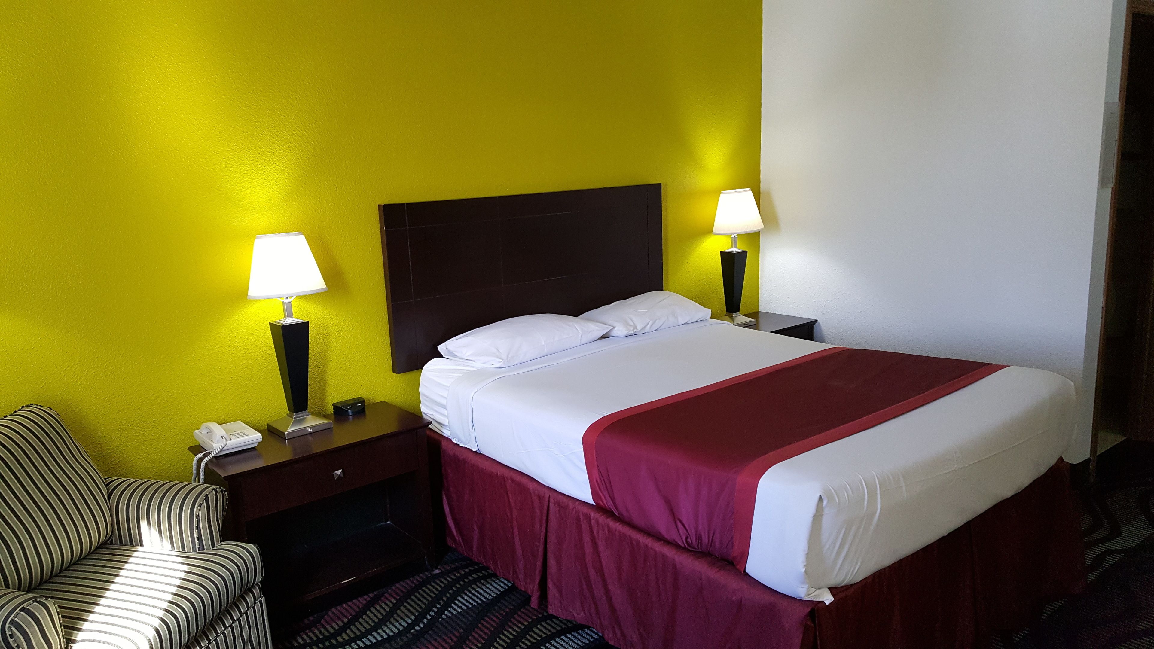 A hotel room with a bed, two bedside lamps, a telephone, and a striped armchair.