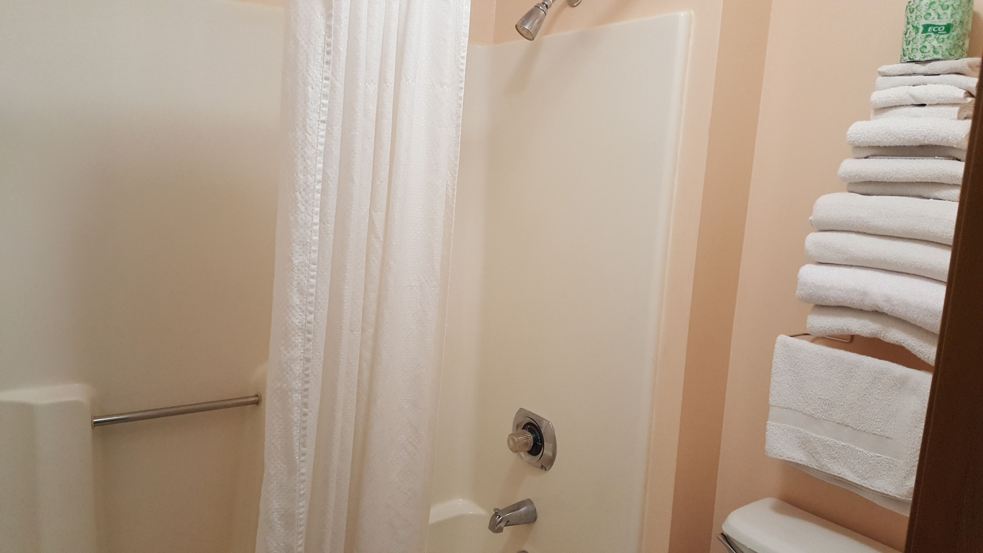 A bathroom with a shower curtain, a towel rack with folded towels, and a toilet.