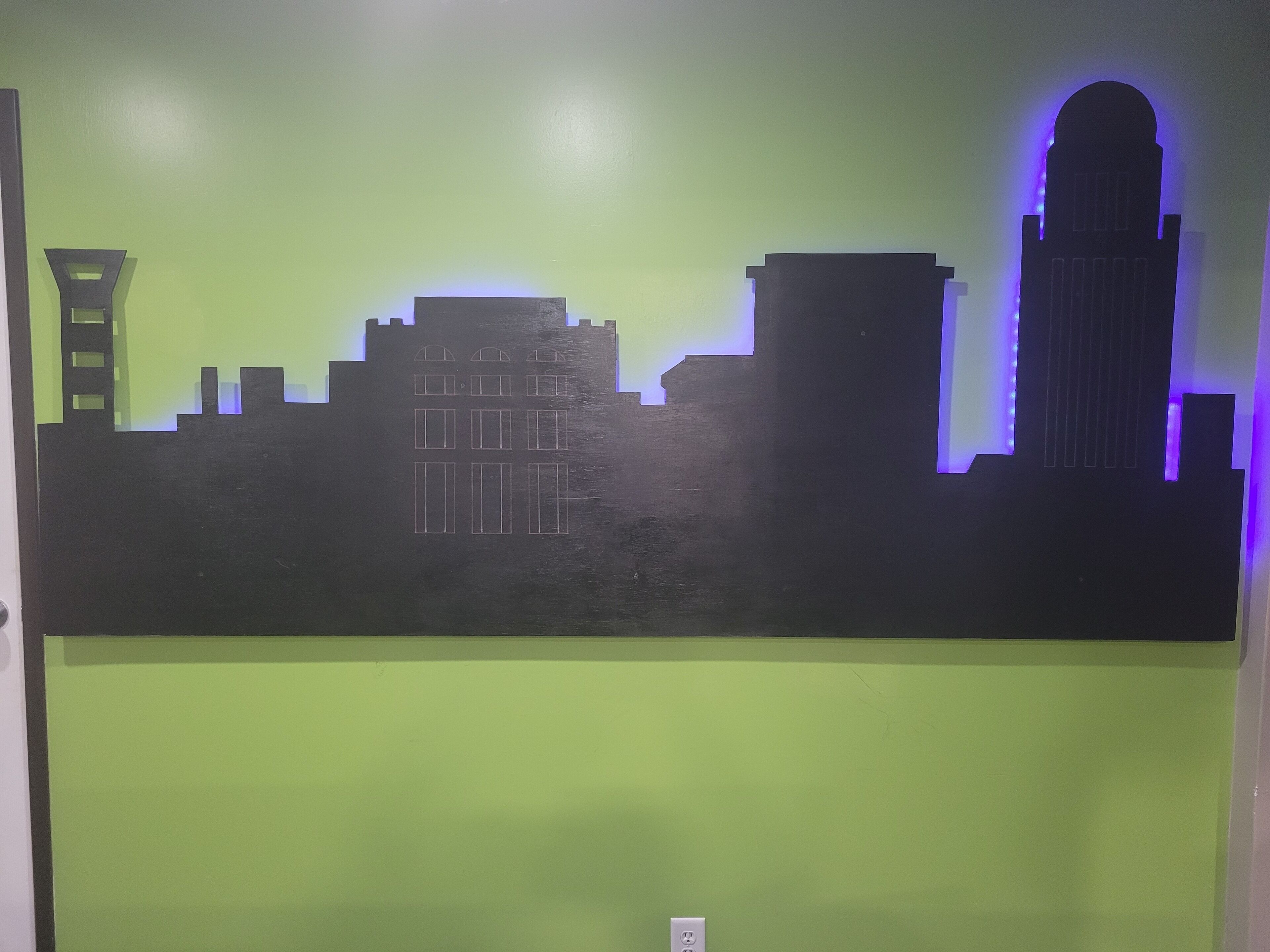 A city skyline silhouette with a green background and a power outlet at the bottom.