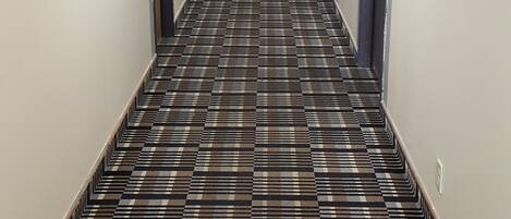 A hotel hallway with a checkered carpet, doors on both sides, and a sign indicating the breakfast room.