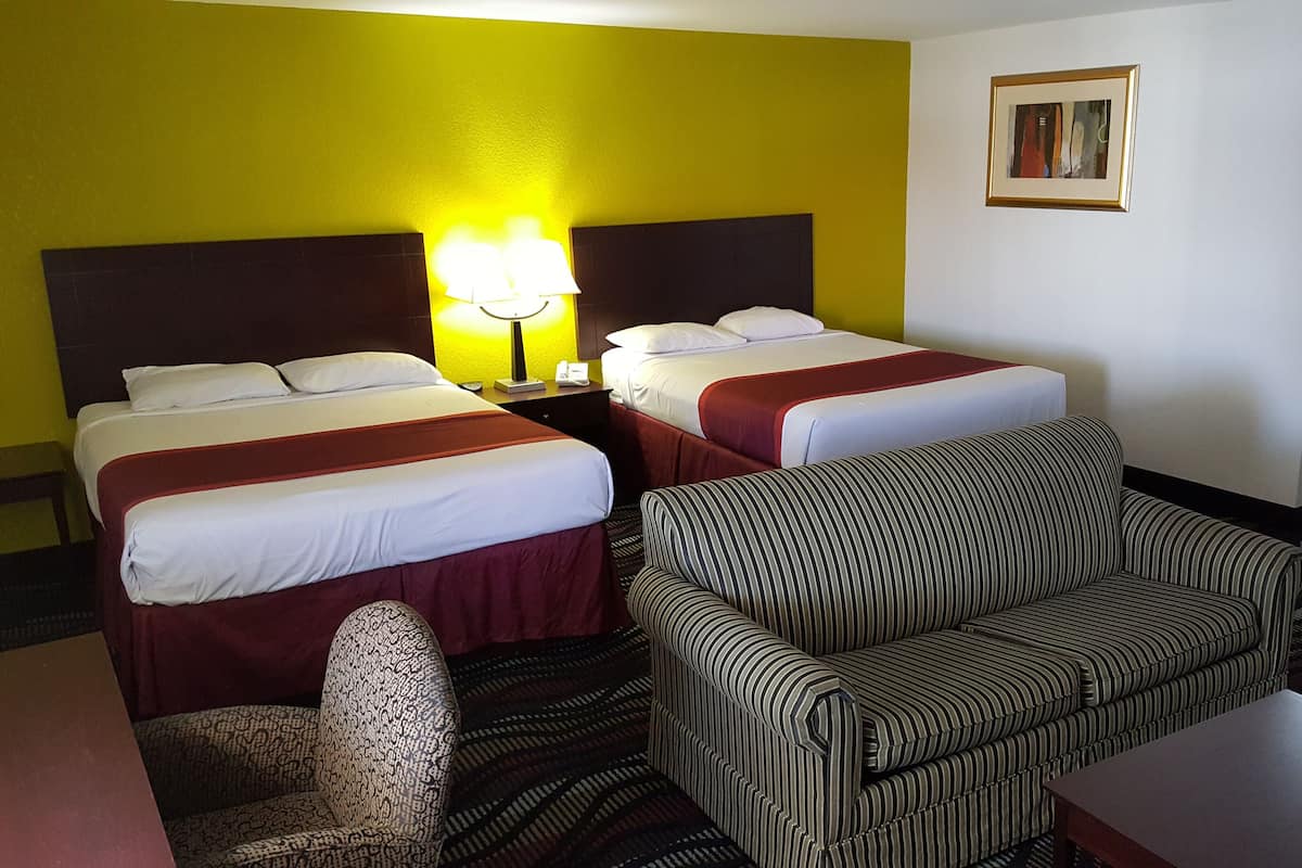 A hotel room with two beds, a sofa, a chair, and a small table.