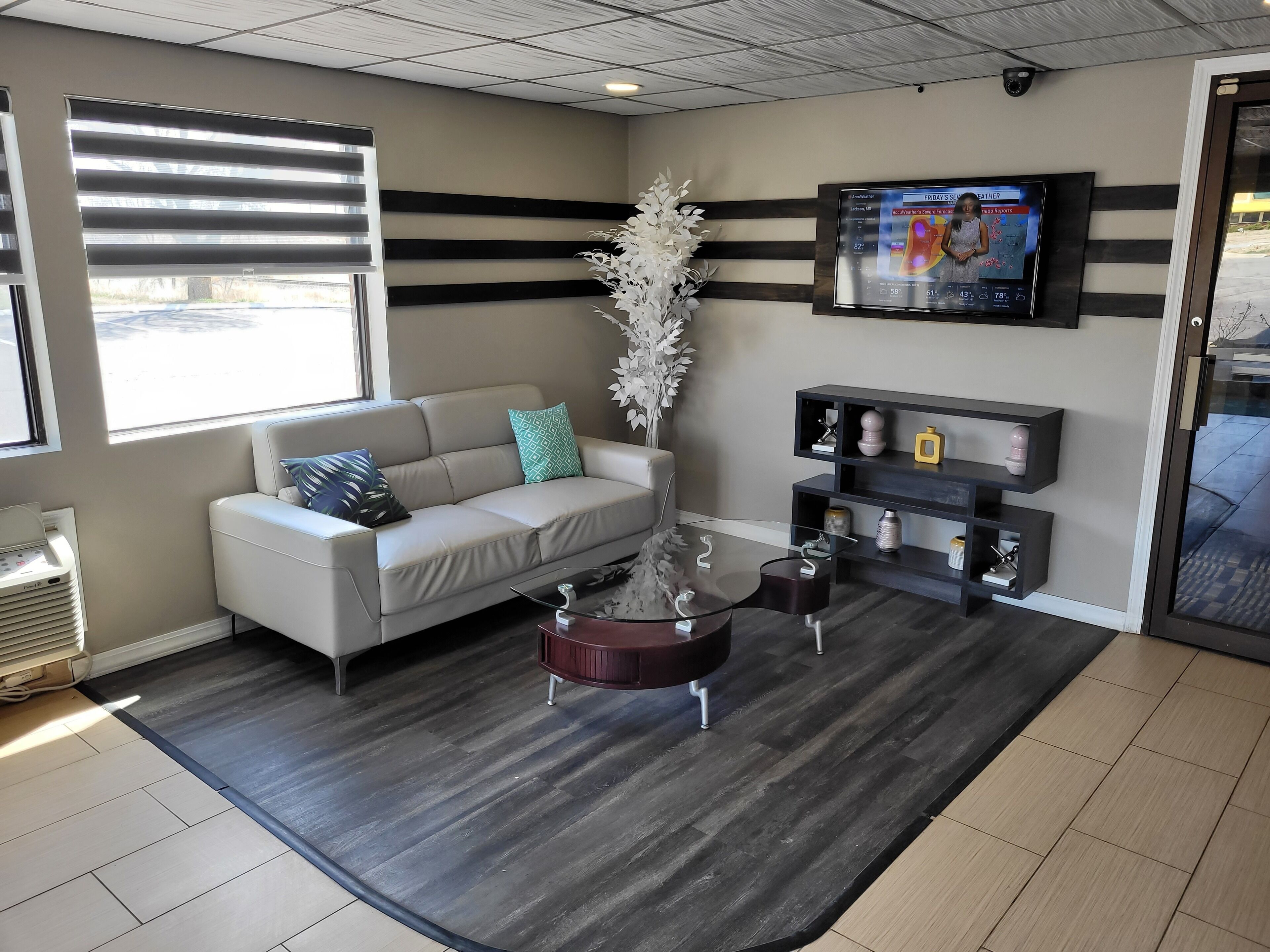A modern waiting area with a sofa, a coffee table, a decorative plant, and a mounted TV displaying weather information.