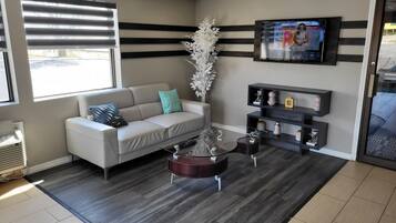 A modern waiting area with a sofa, a coffee table, a decorative plant, and a mounted TV displaying weather information.