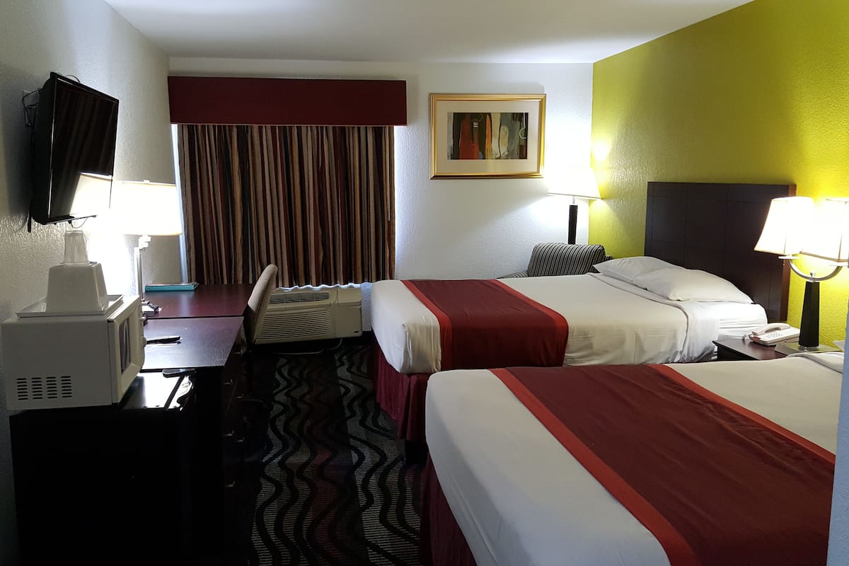 A hotel room with two beds, a desk, a chair, a TV, a painting, and a lamp.