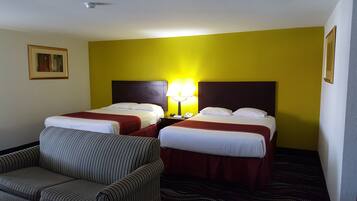 Habitación de hotel con dos camas, una silla y una lámpara.