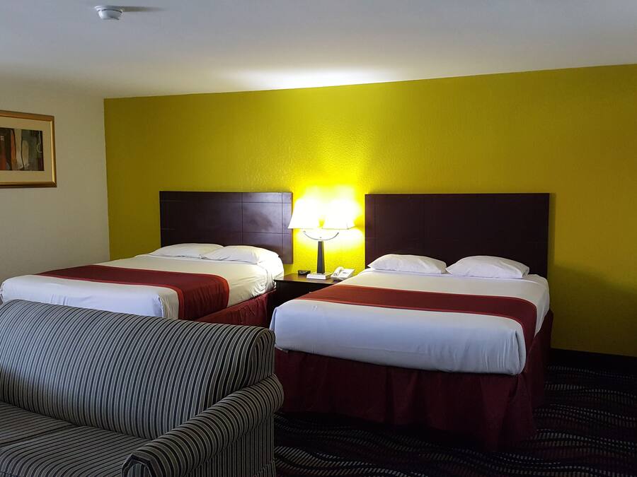 Habitación de hotel con dos camas, una silla y una lámpara.