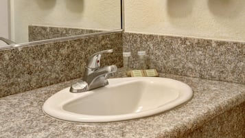 Ein Badezimmerwaschbecken mit einer Granit-Arbeitsplatte, ein Spiegel darüber und zwei Seifenspendern auf der Platte.