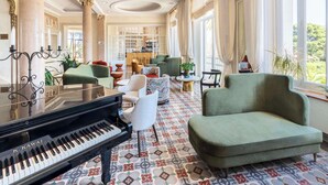 Un salón majestuoso con un piano de cola, asientos cómodos, ventanas amplias y un suelo decorado con mosaicos.