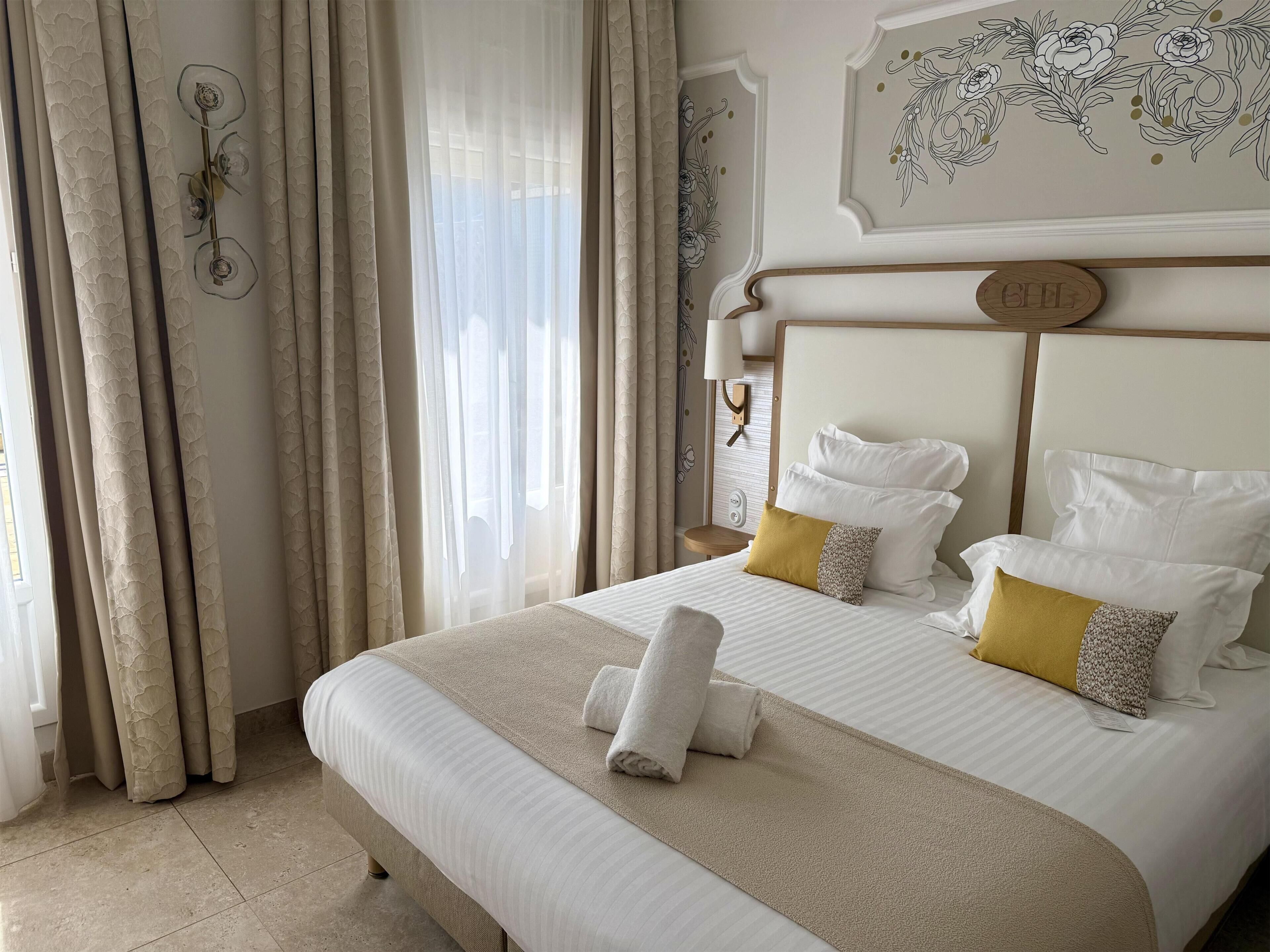 Una habitación de hotel con una cama, cortinas, una lámpara de pared y un adorno mural.