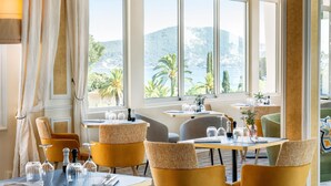 Un comedor con sillas amarillas, una mesa con copas de vino y vistas a un paisaje montañoso a través de grandes ventanales.