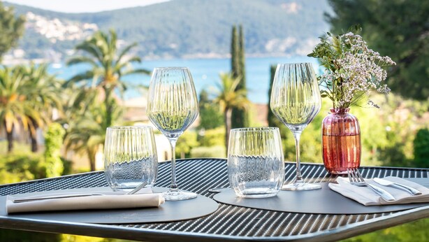 Mesa dispuesta con copas de vino y un jarrón de flores, con vista a un paisaje costero.