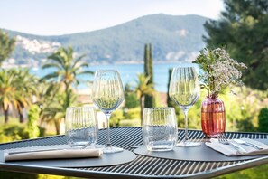 A table set with wine glasses and a vase of flowers, overlooking a scenic coastal view. - Grand Hotel Des Lecques, BW Signature Collection (Saint-Cyr-sur-Mer)